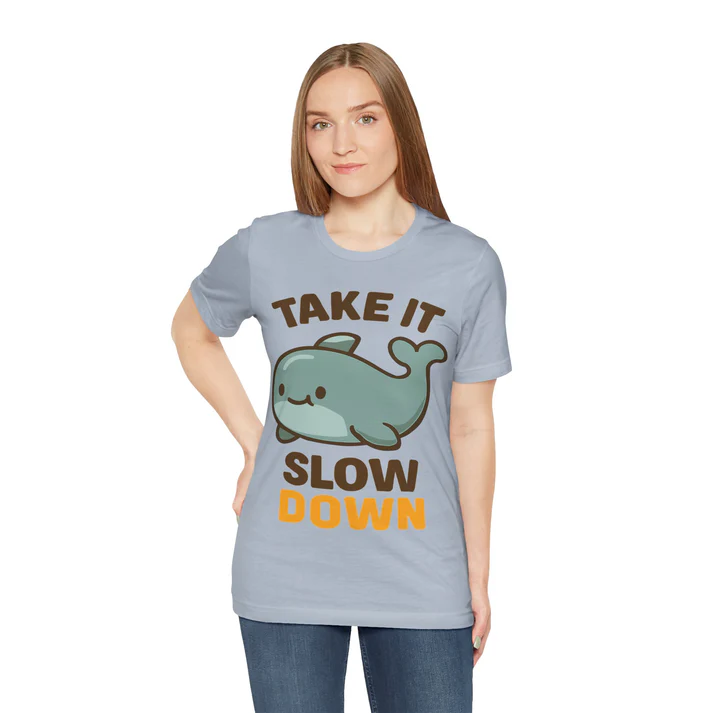 Woman wearing a light blue t-shirt featuring a cute whale graphic and the text "TAKE IT SLOW DOWN," promoting a relaxed lifestyle.