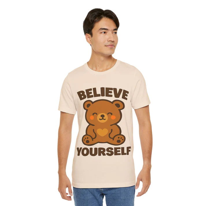 Cream-colored t-shirt featuring a cartoon bear and the motivational phrase "Believe Yourself," worn by a young man, promoting positivity and self-affirmation.